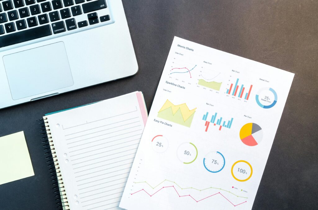 pexels-photo-669619-669619 Flatlay of business report with colorful charts, a notebook, and a laptop for data analysis on a desk.
