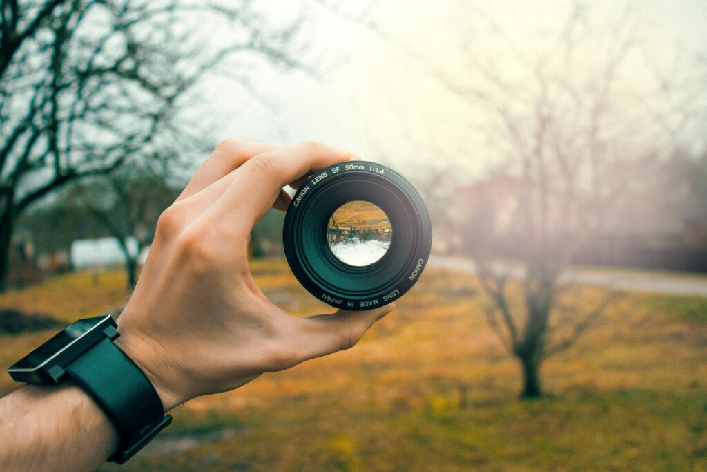 pexels-photo-759960-759960 Close-up of a hand holding a 50mm camera lens outdoors, focusing through the lens.